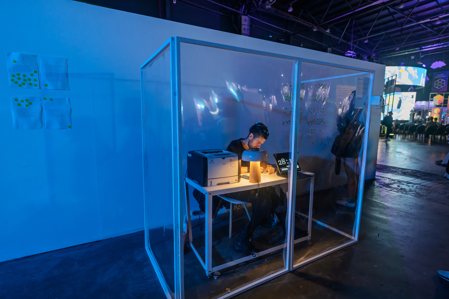 Artist working at a desk inside the transparent cube installation