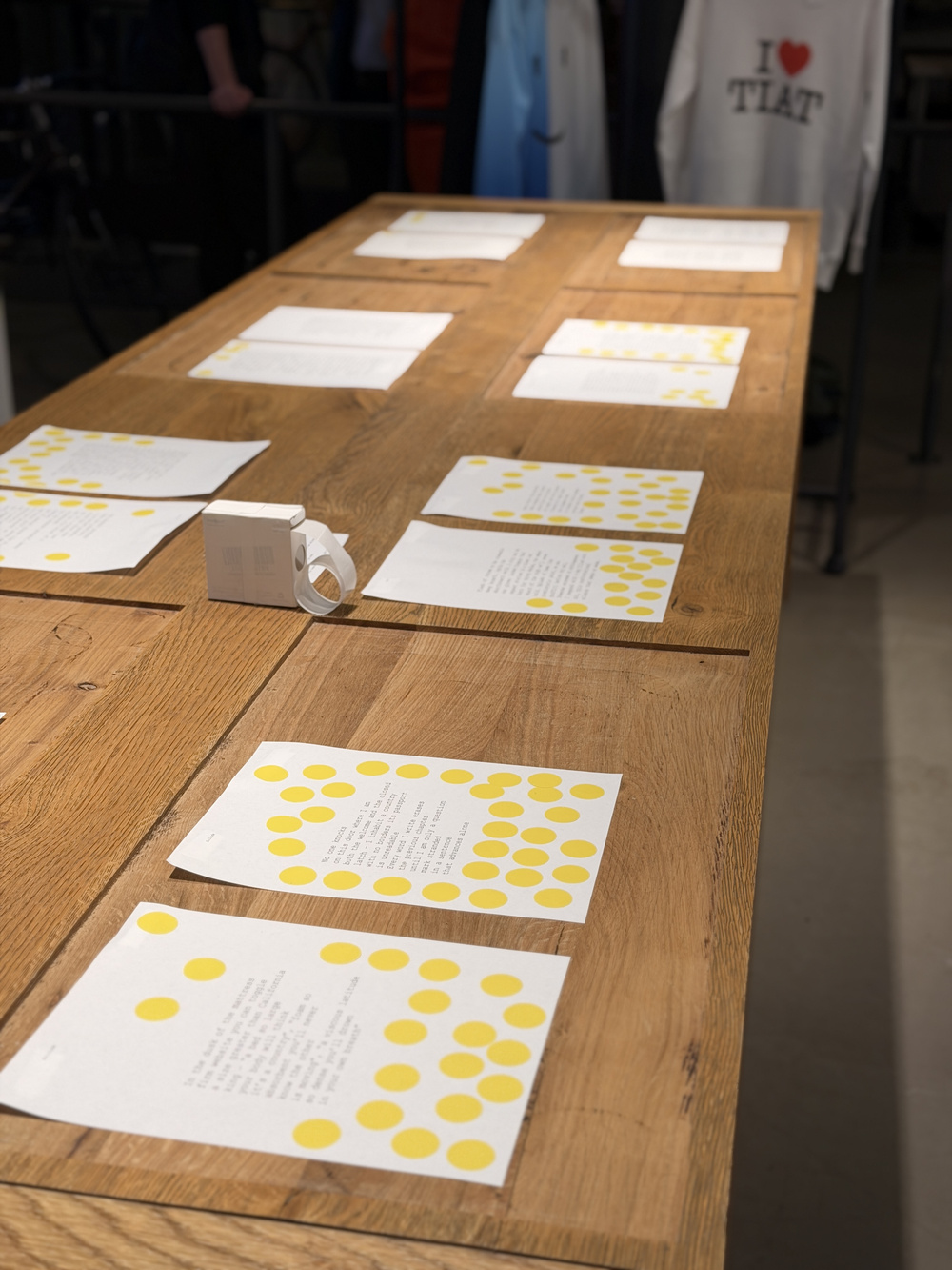 Poems with yellow voting dots spread across a wooden table at TIAT